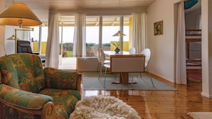 A living room with a patterned sofa, a fluffy rug, a dining table with chairs, and a view through large windows. - Lovely home in Kalundborg with kitchen (Kalundborg)