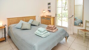 Un dormitorio con cama, almohadas, mesita de noche, cómoda, silla, ventana y espejo.