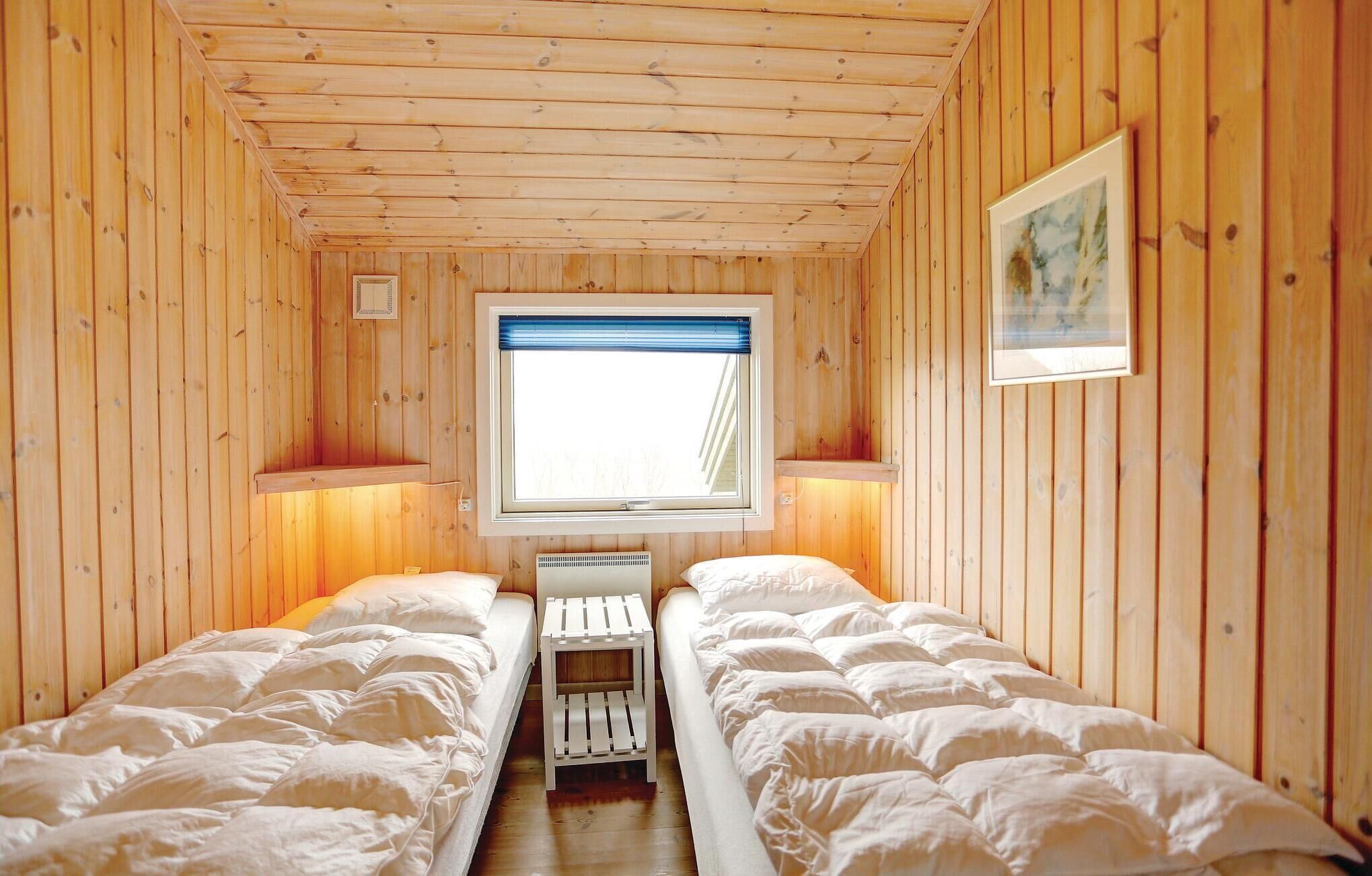 Een kleine, gezellige kamer met houten wanden en een raam met een blauwe luik. Er staan twee bedden met witte lakens en een klein tafeltje ertussen.