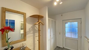 Une pièce comprenant une commode en bois, un miroir, un porte-manteau mural, une plante en pot et une porte dont les panneaux sont en verre dépoli.