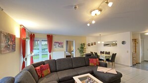 Un salon moderne avec un canapé d’angle, une table basse en verre et un coin repas comprenant une table et des chaises.