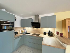 Cozinha compacta com armários cinzentos, forno embutido, micro-ondas, pia e bancada de madeira.