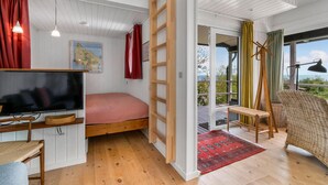 Ein gemütliches Zimmer mit einem Bett, einem Schreibtisch mit Stuhl, einem Fernseher und einem großen Fenster mit Vorhängen.