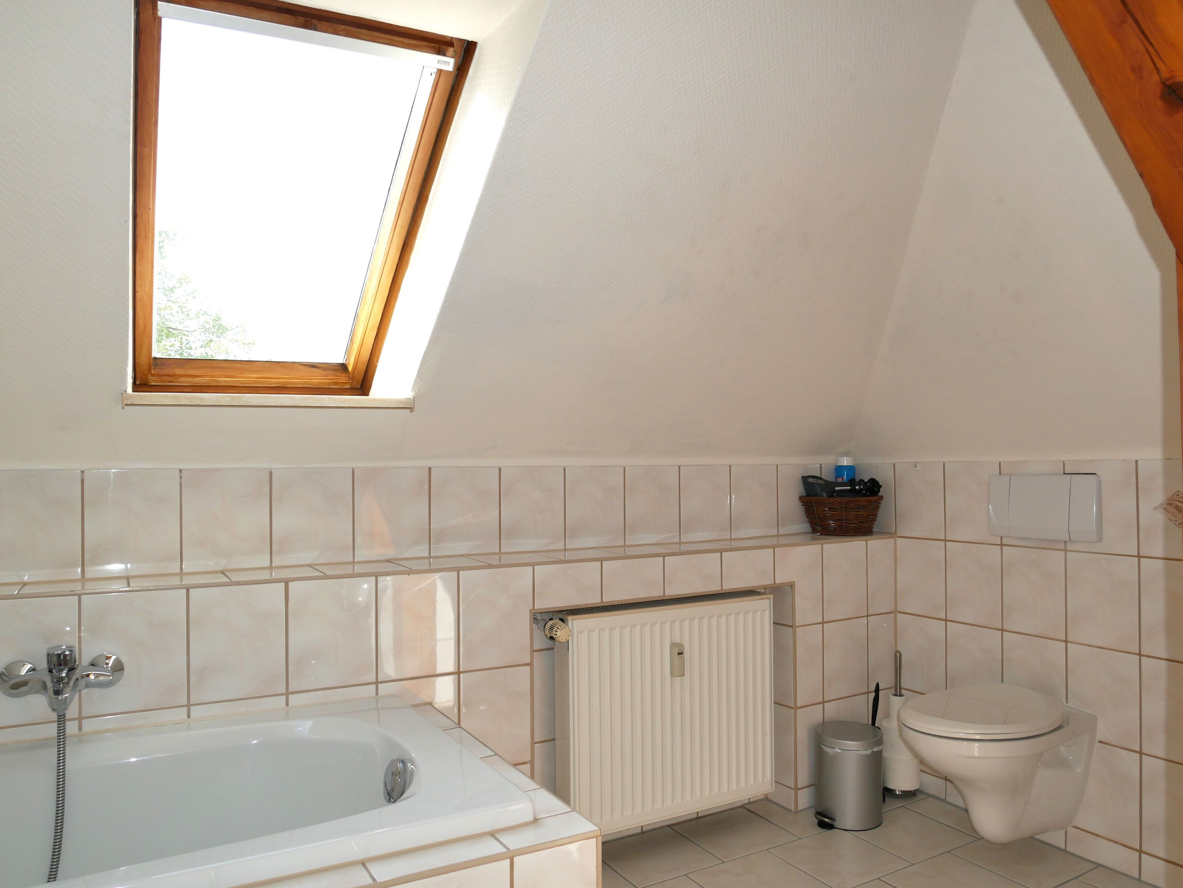 A bathroom with a bathtub, toilet, radiator, and a window.