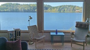 A room with a large window overlooking a lake and forest. There are two chairs, a small table, and a lamp. - Beautiful home in Smålandsstenar (Smålandsstenar)