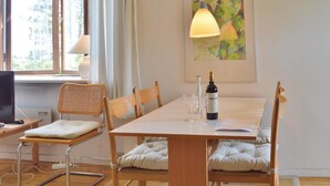 A dining area with a wooden table, cushioned chairs, a bottle of wine, and a painting on the wall. - 1 bedroom stunning apartment in Hornbæk (Hornbæk)
