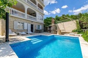 Un edificio de dos pisos con piscina, asientos al aire libre y un muro de piedra.
