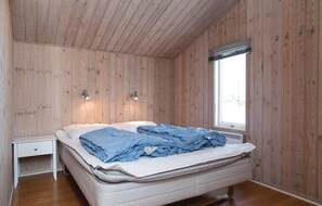 Una camera da letto con pareti in legno, un letto con biancheria blu, un comodino e due luci fissate al muro.