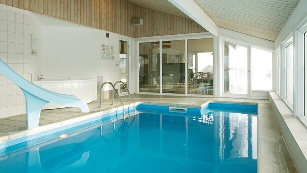 An indoor swimming pool with a slide, glass doors leading to a dining area, and a wooden ceiling. - Amazing home in Løkken with sauna (Løkken)