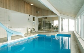 Una piscina interna con uno scivolo, porte vetrate che conducono a una sala da pranzo e un soffitto in legno.