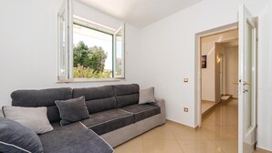 Una sala moderna con un sofá seccional gris, un ventanal con vistas a la vegetación y un pasillo que conduce a otra habitación.