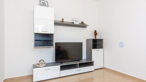 Una sala de estar moderna con un televisor de pantalla plana, muebles blancos y objetos decorativos en estantes.