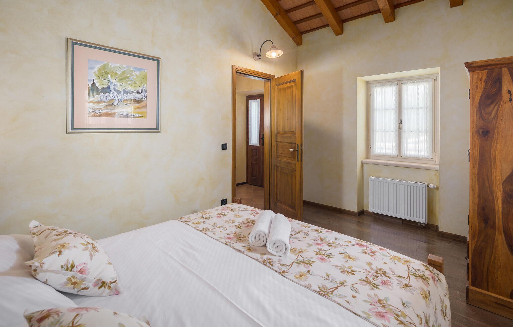A bedroom with a bed, a wooden wardrobe, a radiator, and a window with curtains.