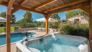 A hot tub under a wooden pergola with a pool and lounge chairs in the background. - Stunning home in Tinjan with sauna (Tinjan)