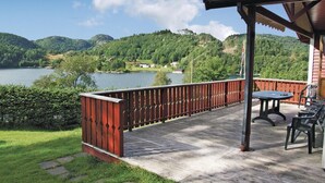Une terrasse en bois avec une rambarde en métal, donnant sur un lac et des collines.