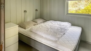 Un lit simple avec un matelas blanc matelassé et deux oreillers, une table de chevet et une fenêtre donnant sur un paysage verdoyant.