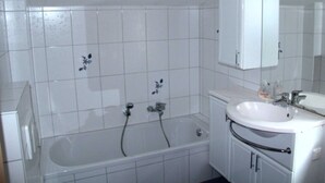 A bathroom with a bathtub, a sink, and a mirror. - Sunshine house in Baabe - holiday home (Baabe)