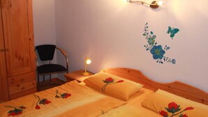 A bedroom with a wooden bed, a chair, a nightstand with a lamp, and a wall with floral and butterfly decals. - Sunshine house in Baabe - holiday home (Baabe)