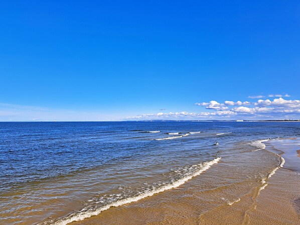 A beach with clear blue water, waves, and a distant ship.