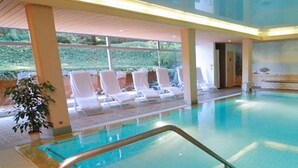 Una piscina interna con pavimento piastrellato, una scala in metallo e confortevoli poltrone da relax bianche.
