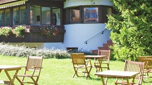 Un edificio a due piani con un balcone fiorito, una scala che conduce al piano superiore e un'area esterna con sedie e tavoli.