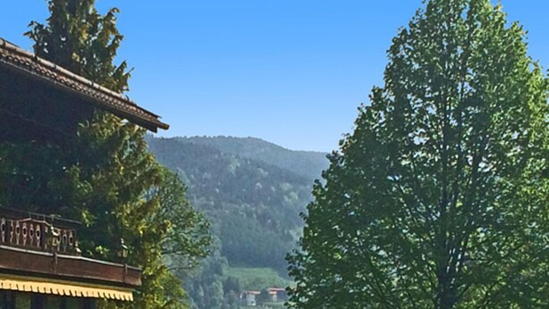 Un edificio tradizionale con un balcone, immerso nel verde e con vista su un lago e montagne.