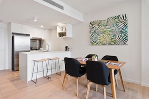 A modern kitchen with a central island, bar stools, and a dining table with chairs. - Ivy and Eve Apartments by CLLIX (South Brisbane)