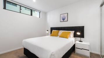 Un dormitorio moderno con una cama grande, una mesita de noche, una lámpara de pared y una ventana.