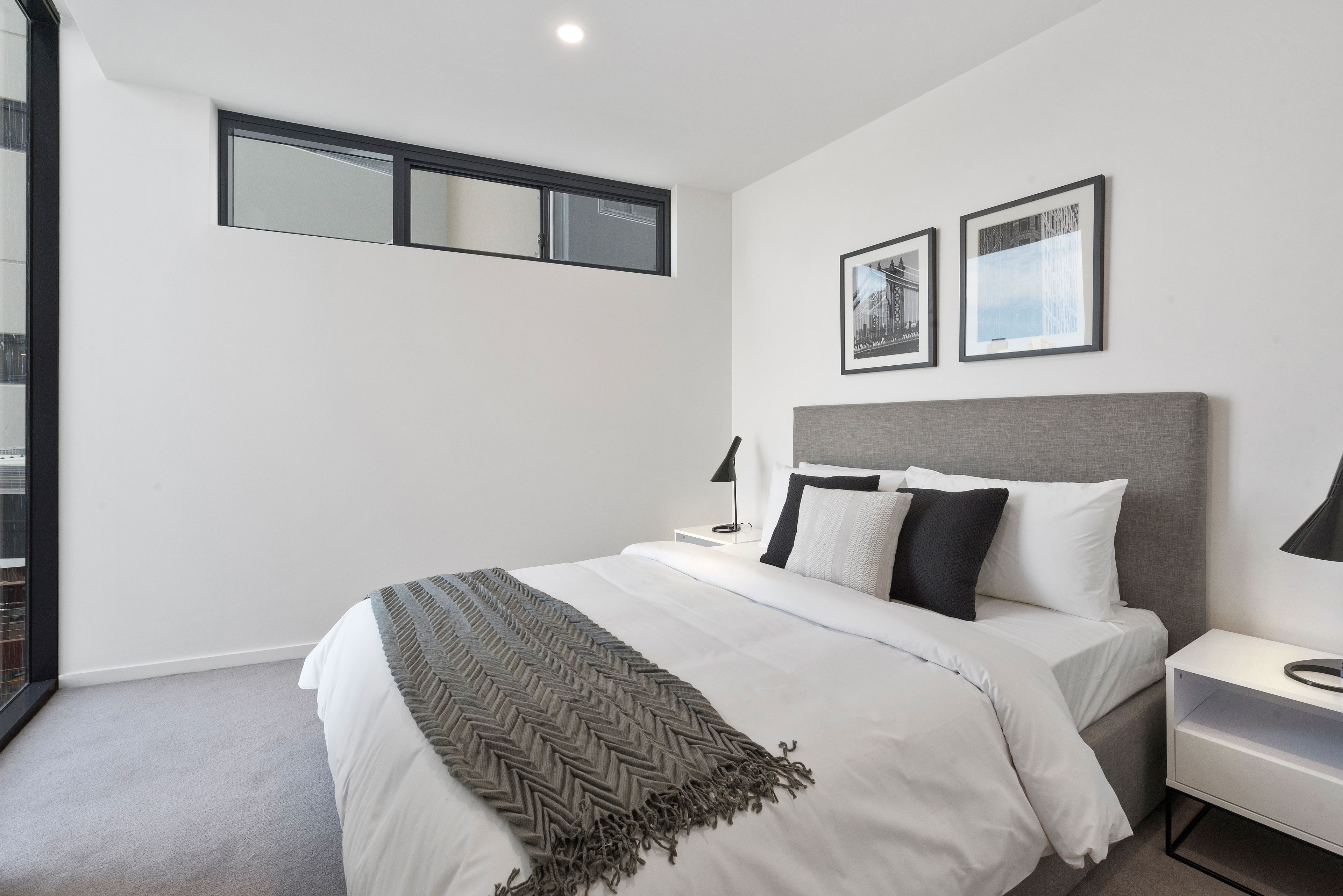 A modern bedroom with a large bed, a grey headboard, and two framed pictures on the wall.