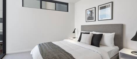Un dormitorio moderno con una cama grande, un cabecero gris y dos cuadros enmarcados en la pared.