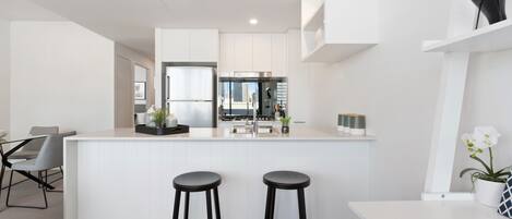 A modern kitchen with white cabinetry, a central island with stools, and a view of the cityscape through the window.