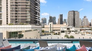 A rooftop pool area with colorful pillows and a city skyline view. - Ivy and Eve Apartments by CLLIX (South Brisbane)