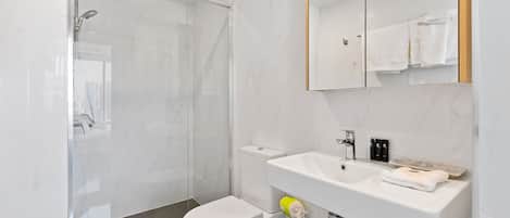 A modern bathroom with a glass-enclosed shower, a white toilet, and a sink with a mirror above it.