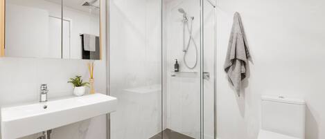 A modern bathroom with a glass-enclosed shower, a white sink, and a toilet.