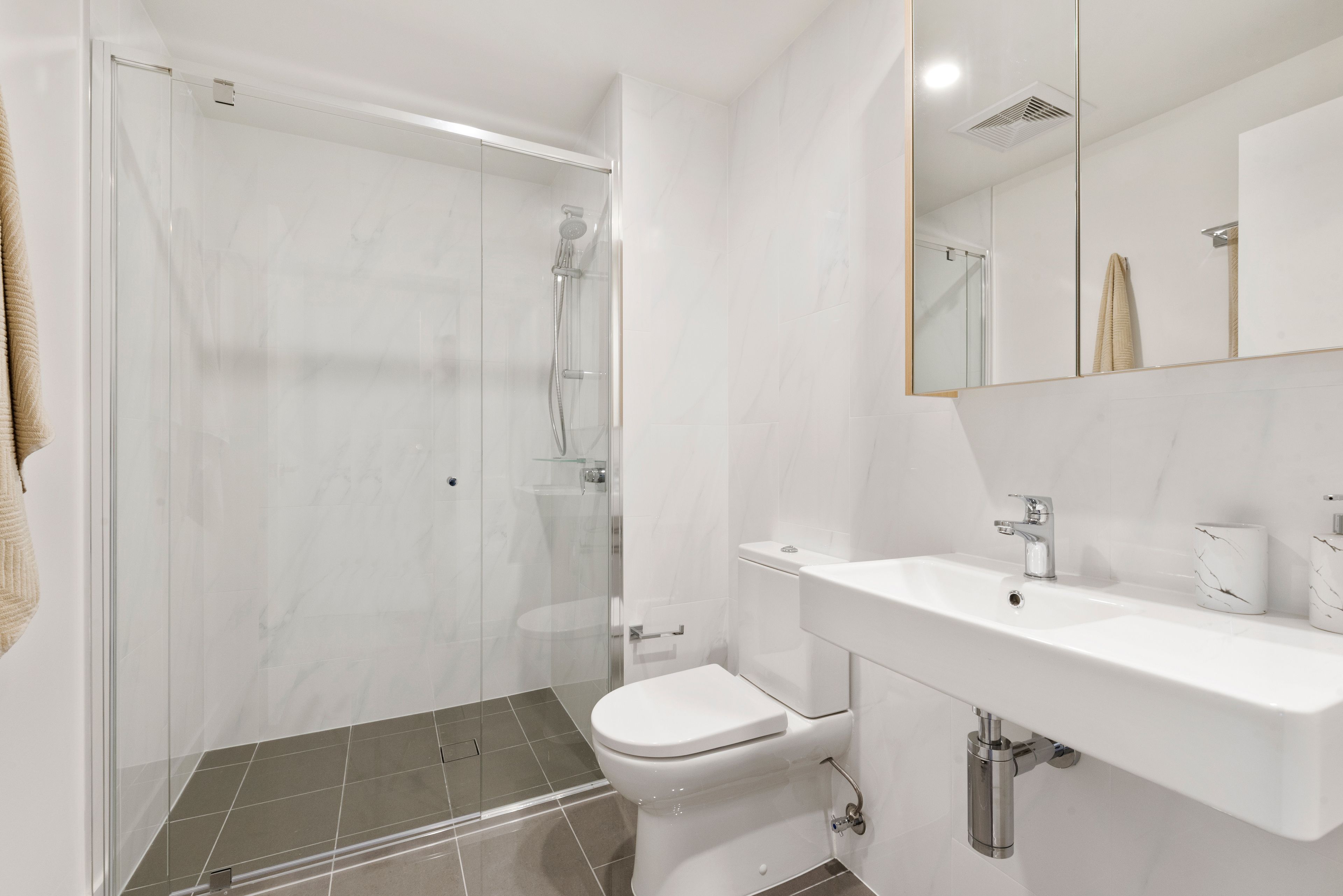 A modern bathroom with a glass-enclosed shower, a white toilet, and a sink with a marble countertop.