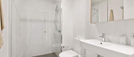 Une salle de bain moderne avec une douche à parois de verre, des toilettes blanches et un lavabo doté d’un plan de travail en marbre.