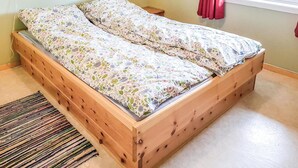 Una cama de madera con ropa de cama floral en una habitación con ventana y cortina roja.