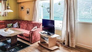 Una sala de estar con un sofá rojo, un televisor sobre un mueble de madera, una mesita con un cuenco y una ventana con cortinas.