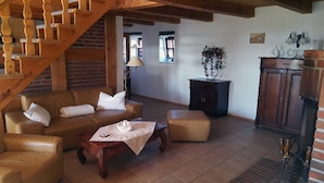 A cozy living room with a brown leather sofa, a wooden coffee table, and a staircase with wooden railings. - Holiday house Rankwitz - holiday house (Rankwitz)