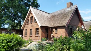 A traditional brick house with a steeply pitched thatched roof, surrounded by lush greenery and a small garden. - Holiday house Rankwitz - holiday house (Rankwitz)