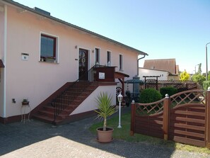 A building with a staircase leading to a door, a small garden area with a potted plant, and a wooden gate. - Bungalow Schumacher in the Ostseebad Zinnowitz - Bungalow (Zinnowitz)