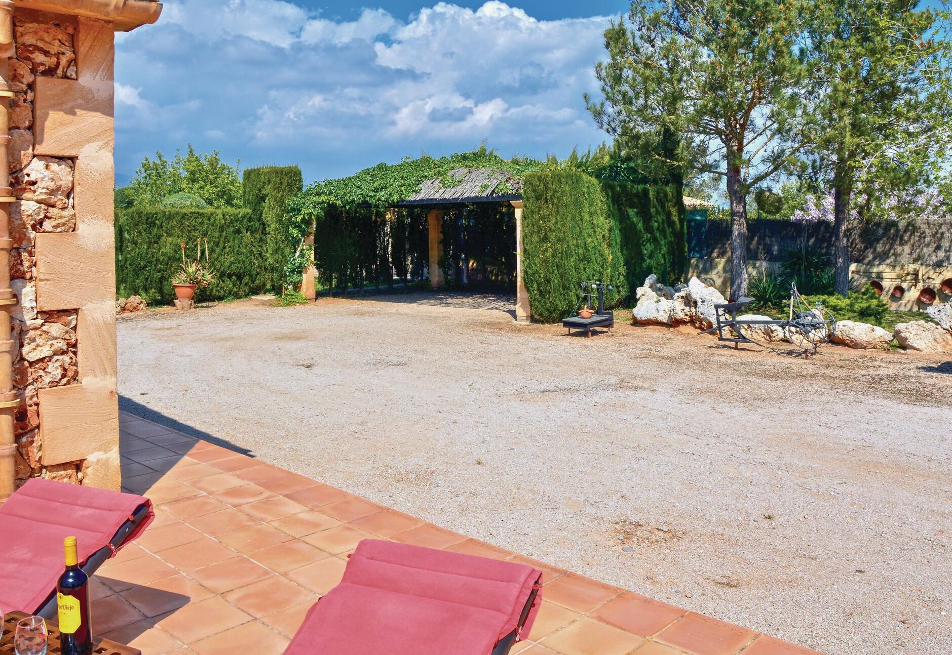 A courtyard with a gravel path, a pergola, and a stone wall.