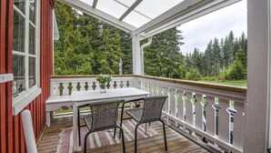 A covered porch with a table and chairs, a vase with flowers, and a view of a forested area. - 3 bedroom stunning home in årjäng (Årjäng)