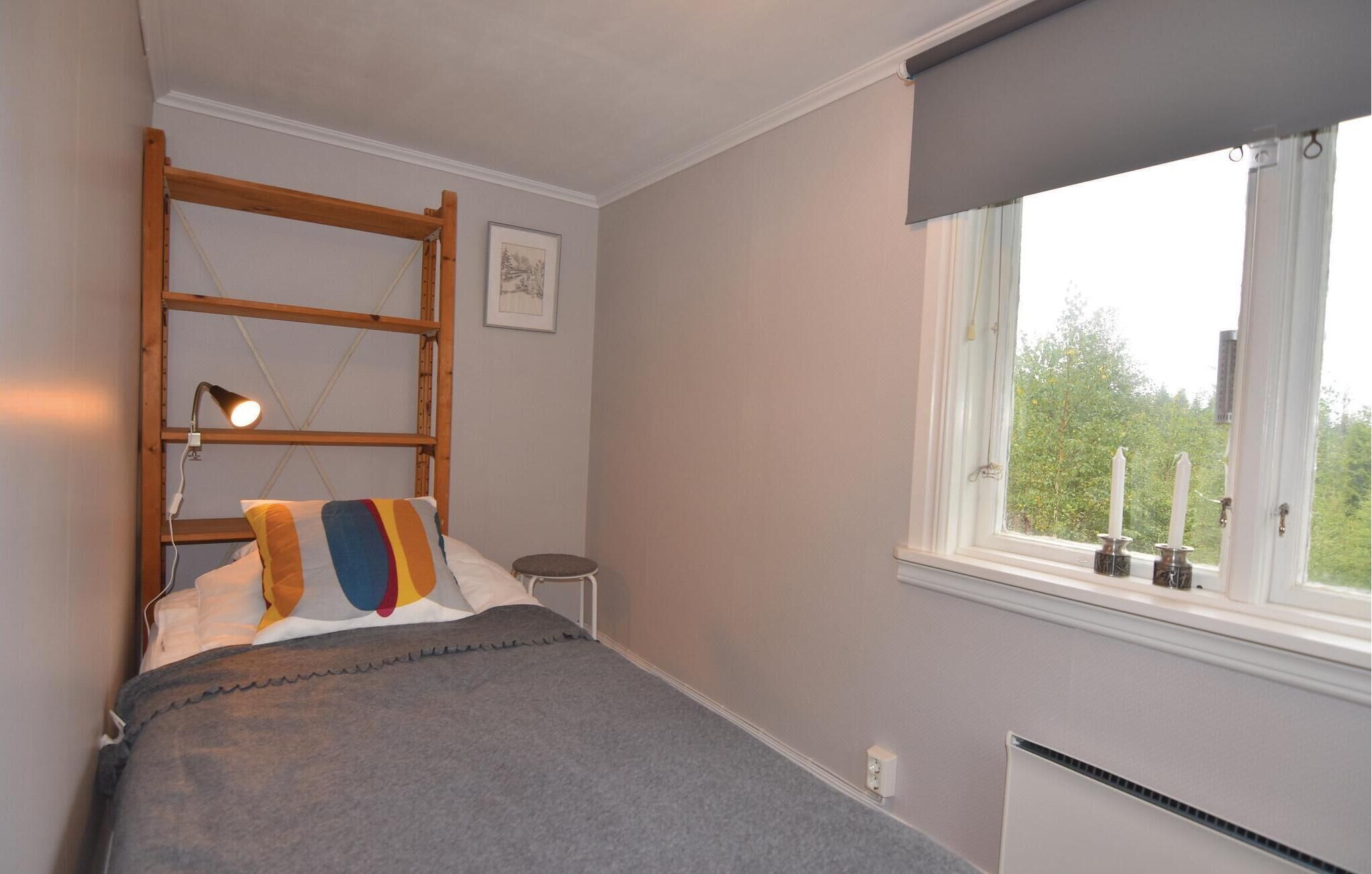 Een slaapkamer met een stapelbed, een bedlampje, een klein krukje en een raam met uitzicht op groen.