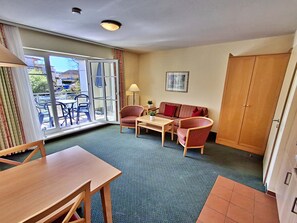 Ein Zimmer mit Esstisch, zwei Stühlen, einer Couch, einer Lampe und einem großen Fenster mit Außenblick.