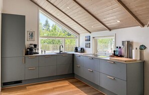 A modern kitchen with grey cabinets, wooden flooring, and large windows offering a view of greenery. - Lovely home in Rømø with sauna (Rømø)