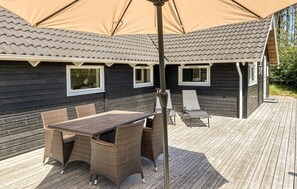 A wooden deck with a table and chairs under a large umbrella, a covered outdoor seating area, and a building with windows and a tiled roof. - Lovely home in Rømø with sauna (Rømø)