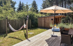 A wooden deck with a hammock, a table with chairs, and a wooden shed. - Lovely home in Rømø with sauna (Rømø)