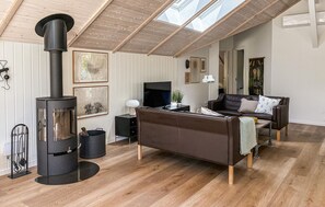 A modern living room with a wood-burning stove, a leather sofa, a flat-screen TV, and a skylight. - Lovely home in Rømø with sauna (Rømø)