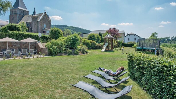 A grassy outdoor area with lounge chairs, a playground, and a church in the background. - Stunning home in Burg Reuland/Steffesh. (Burg Reuland/Steffesh.)